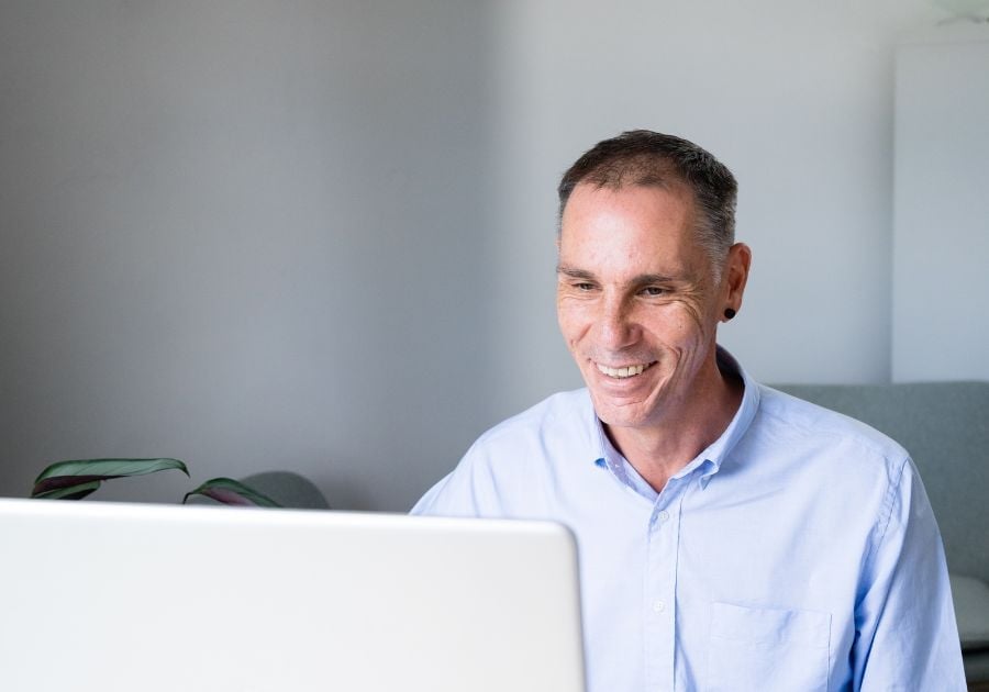 male practitioner sitting in clinic looking at laptop smiling