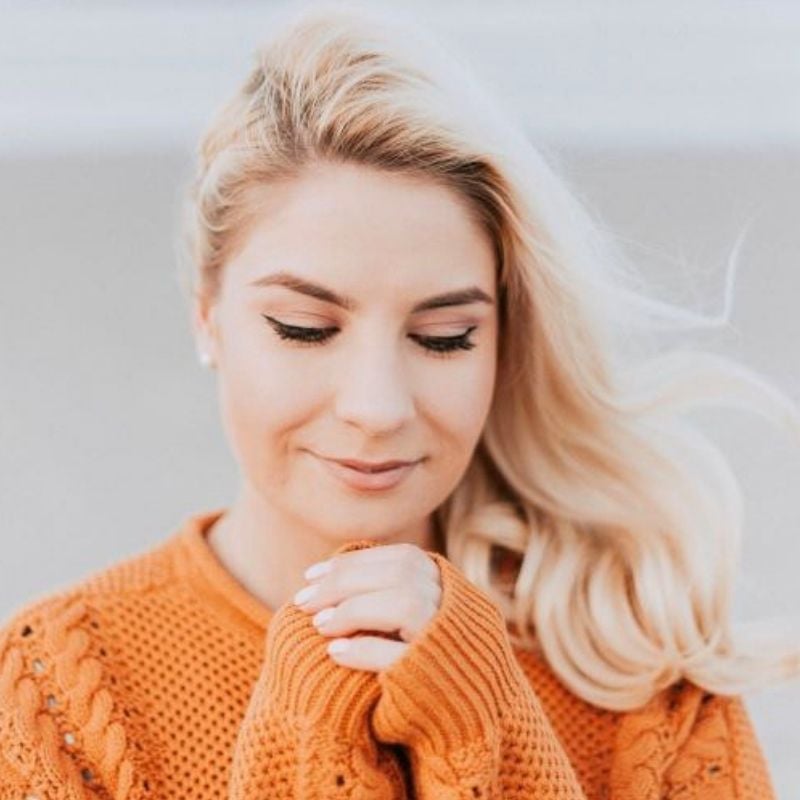 young woman outside wearing orange knit jumper looking down