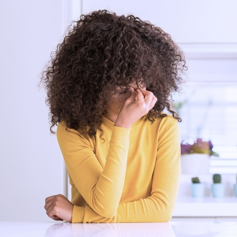 young woman sitting at bench head in hands pinching bridge of nose