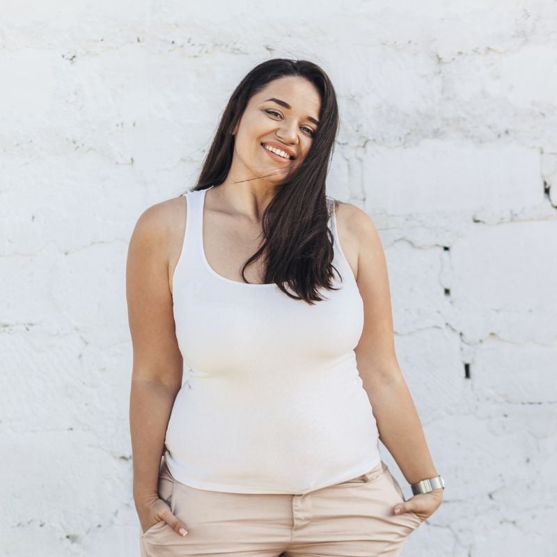 middle aged woman with healthy skin standing outside in front of white brick wall smiling