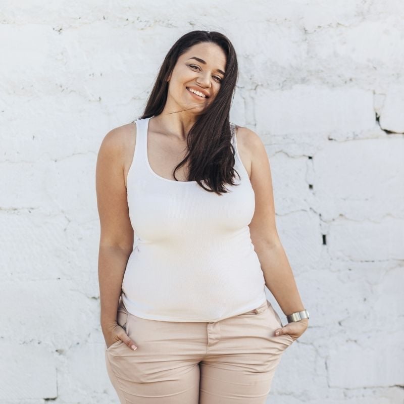 middle aged woman with healthy skin standing outside in front of white brick wall smiling