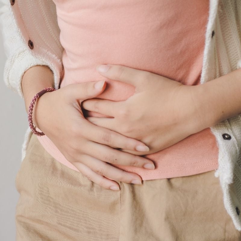 bloating-functional-medicine-condition young woman holding hands across bloated stomach