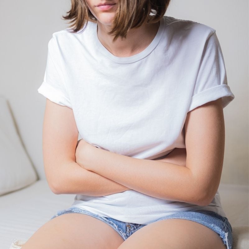 candida-functional-medicine-condition young woman sitting with arms folded across stomach