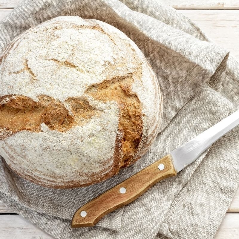 coeliac-functional-medicine-condition round cob of fresh bread containing gluten presented on linen napkin beside bread knife