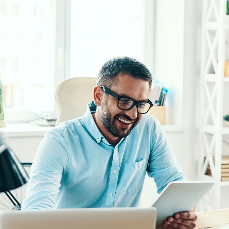 constipation-functional-medicine-hero middle aged man sitting in bright office looking at tablet device and smiling