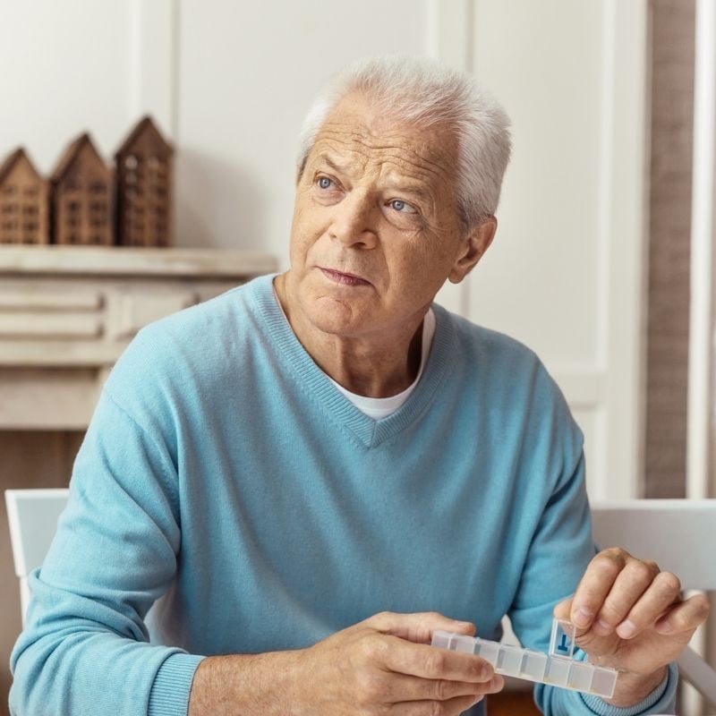 mature man smiling sitting at outdoor table with take away coffee reading book