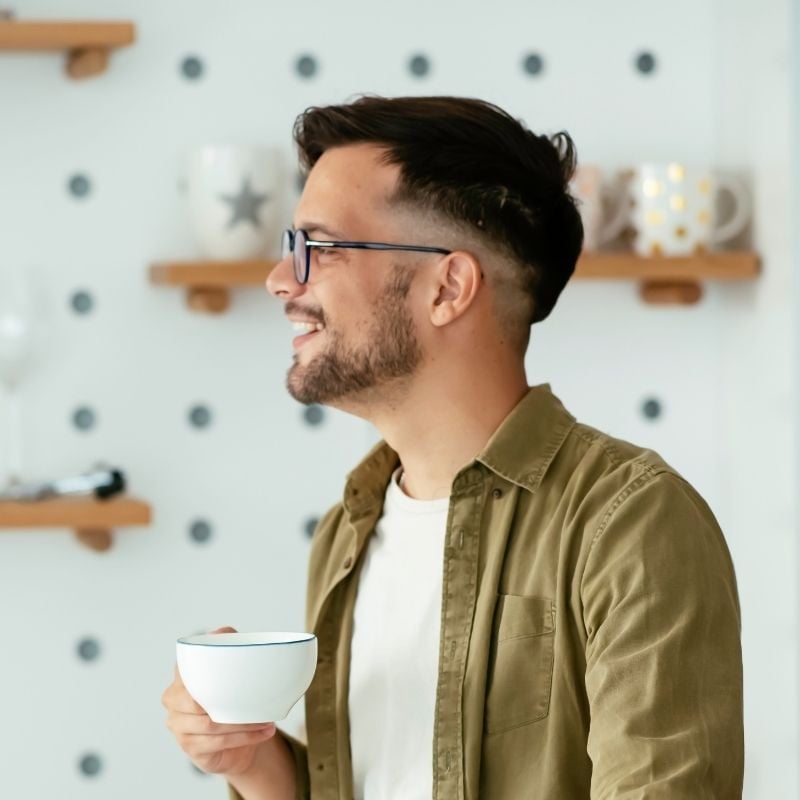 middle aged man holding cup of tea smiling looking out window