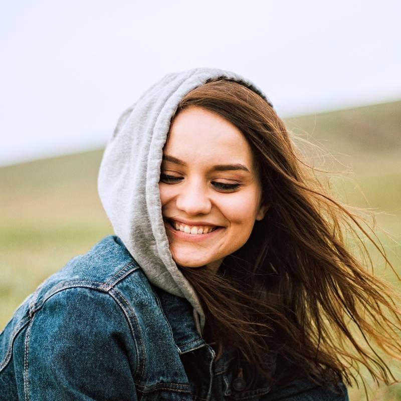 woman outside denim jacket with hood on green hill in background