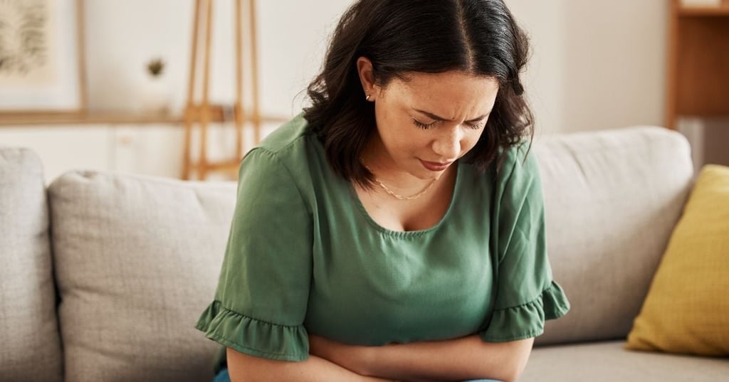 woman leaning forward arms wrapped around stomach frowning sitting on sofa
