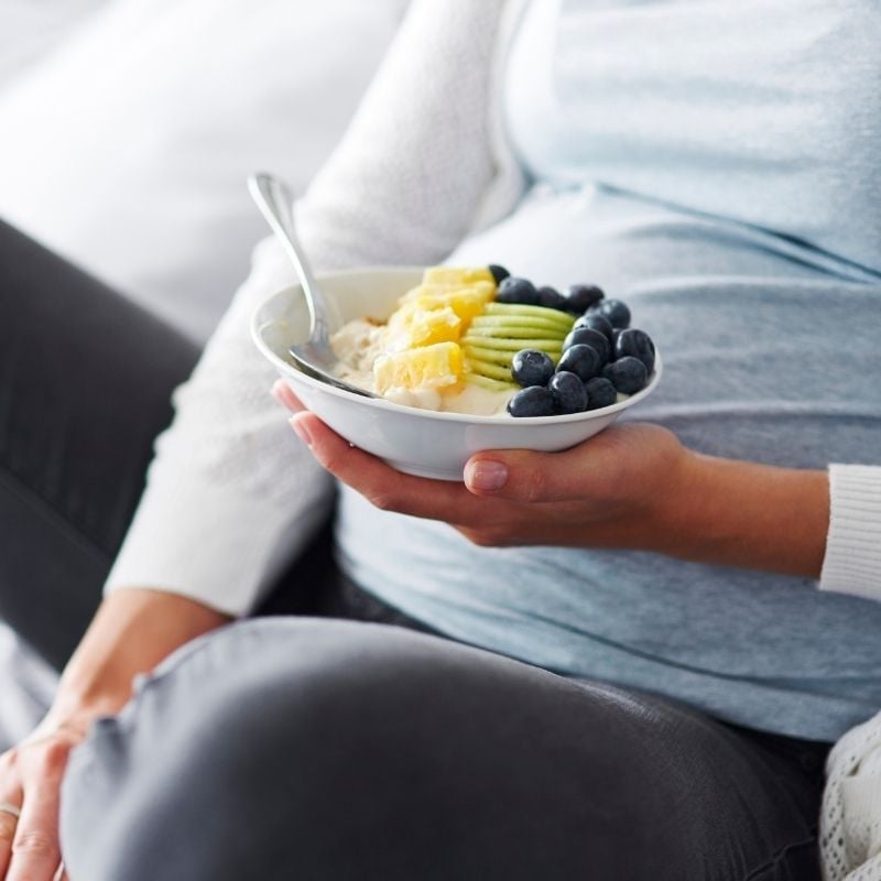 middle aged woman sitting on couch holding bowl of fresh chopped fruit