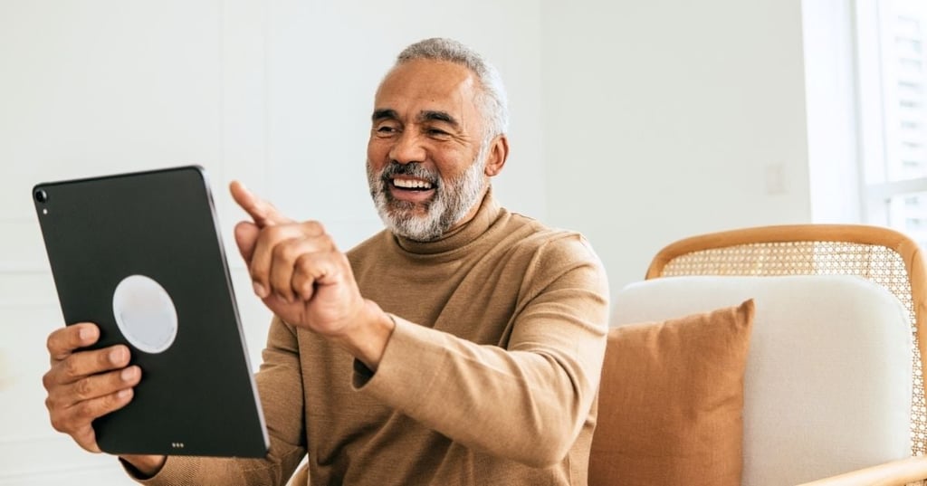 functional-medicine-cost-benefit-hero older man sitting in armchair smiling holding pointing at tablet device at arms length