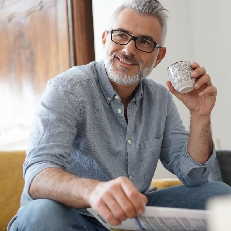 middle aged man sitting on couch with cup of coffee smiling