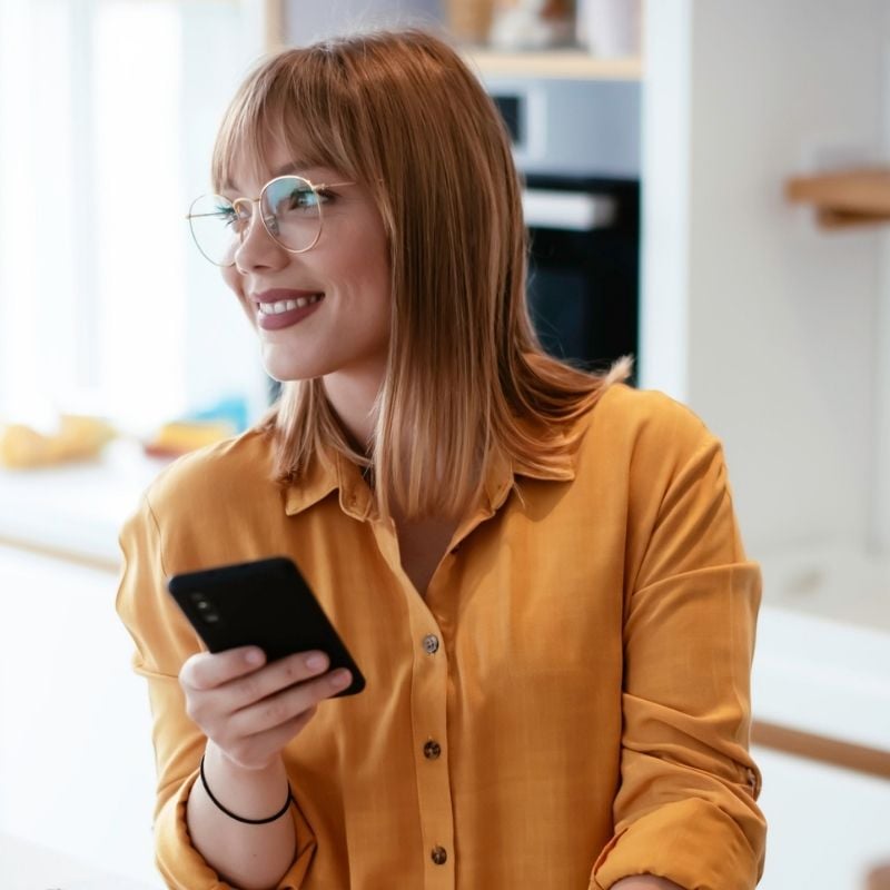 gastroparesis-functional-medicine-hero young woman holding mobile phone in one hand glancing out window smiling