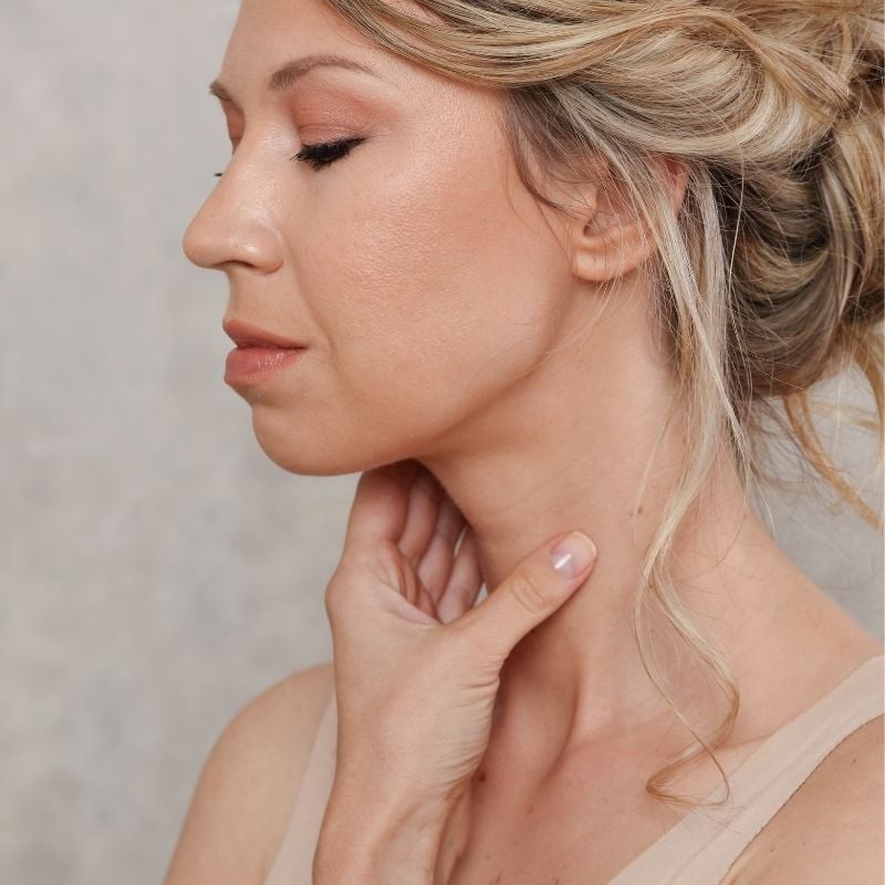 hashimotos-thyroiditis-functional-medicine-condition side profile middle aged woman look downward holding front of neck