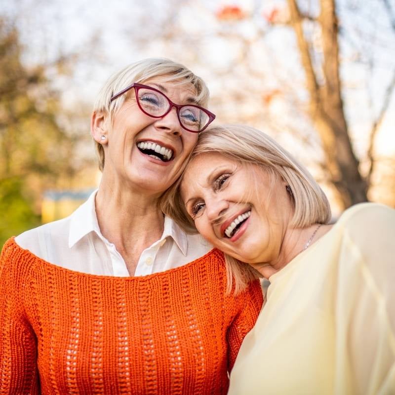 two mature women standing outside heads affectionately resting into one another