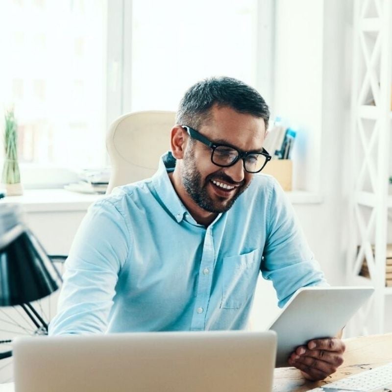 high-cholesterol-functional-medicine-hero middle aged man sitting in bright office looking at tablet device and smiling