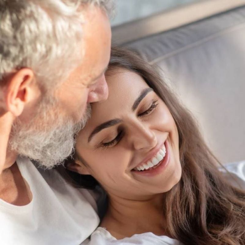 middle aged man sitting on couch kissing forehead of woman who is smiling