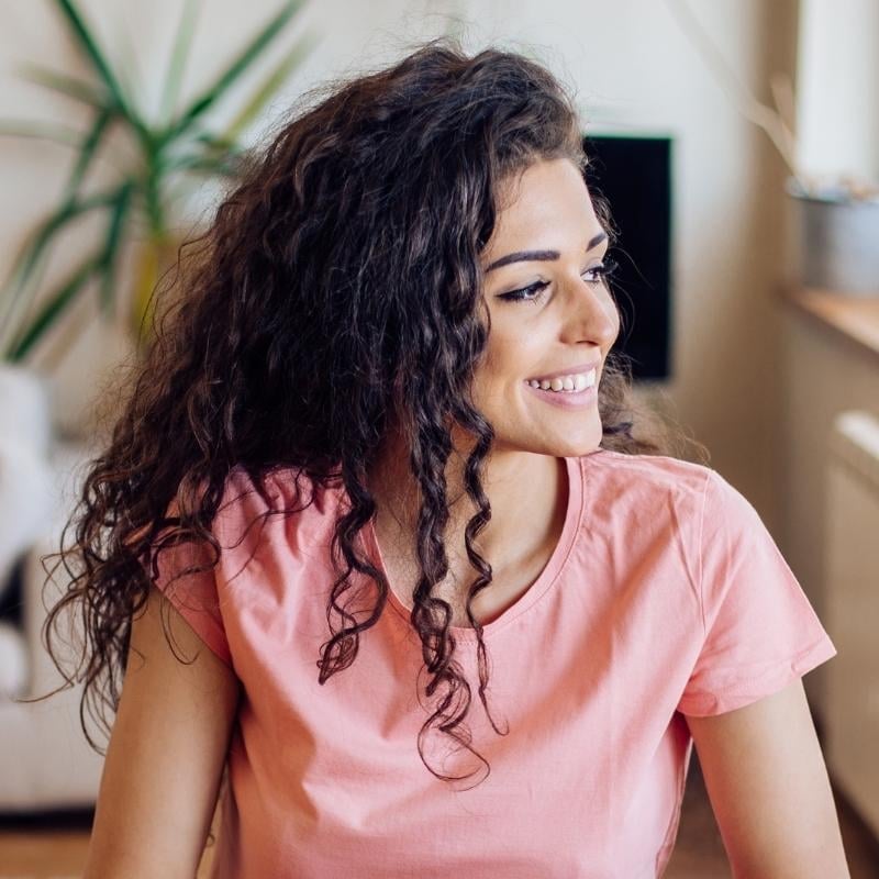 hyperthyroidism-functional-medicine-root-cause vibrant young woman long curly hair smiling looking out the window
