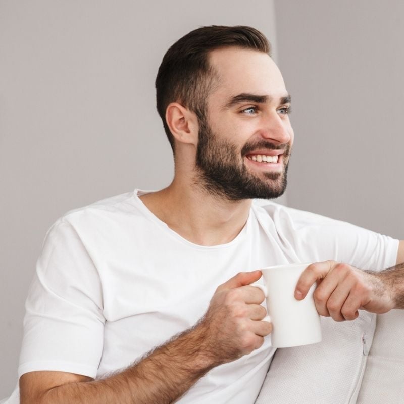 hypotension-functional-medicine-cause middle aged man sitting sideways with arm over back of couch looking out window smiling holding cup of tea