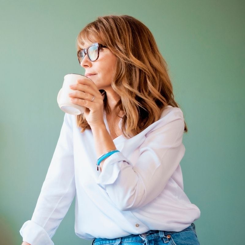 hypotension-functional-medicine-condition mature woman sitting looking out window holding cup of tea up to mouth with one hand
