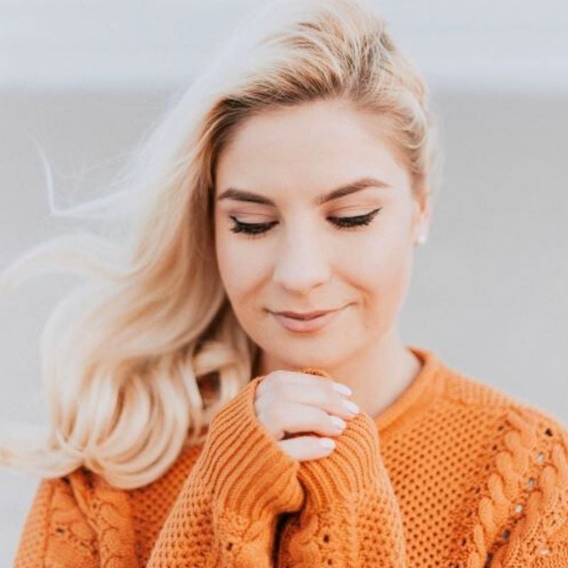 young woman hands clasped just below chin looking down smiling gently