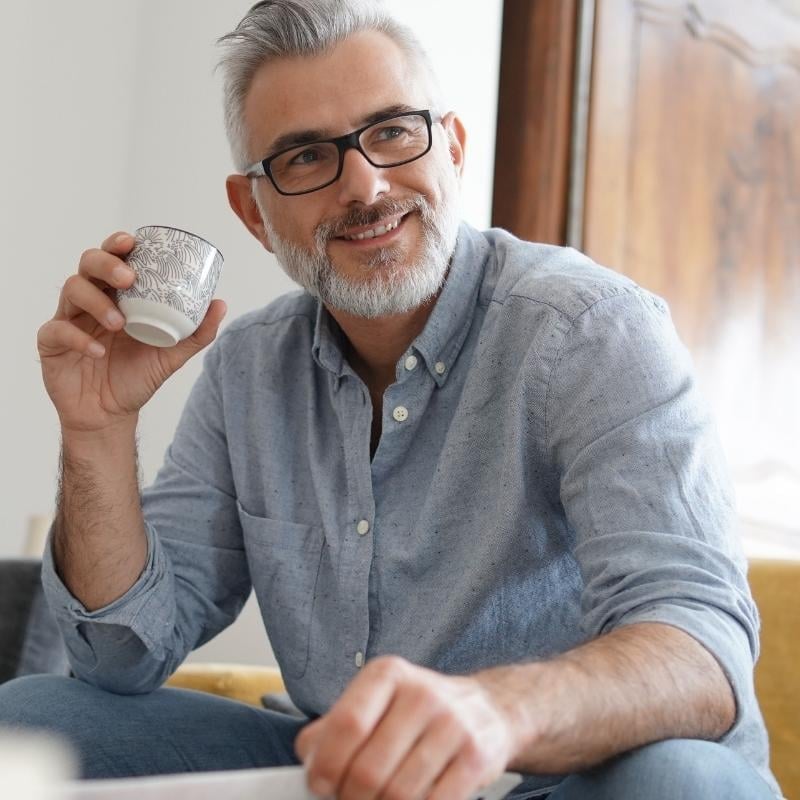 middle aged man sitting on couch with cup of coffee smiling