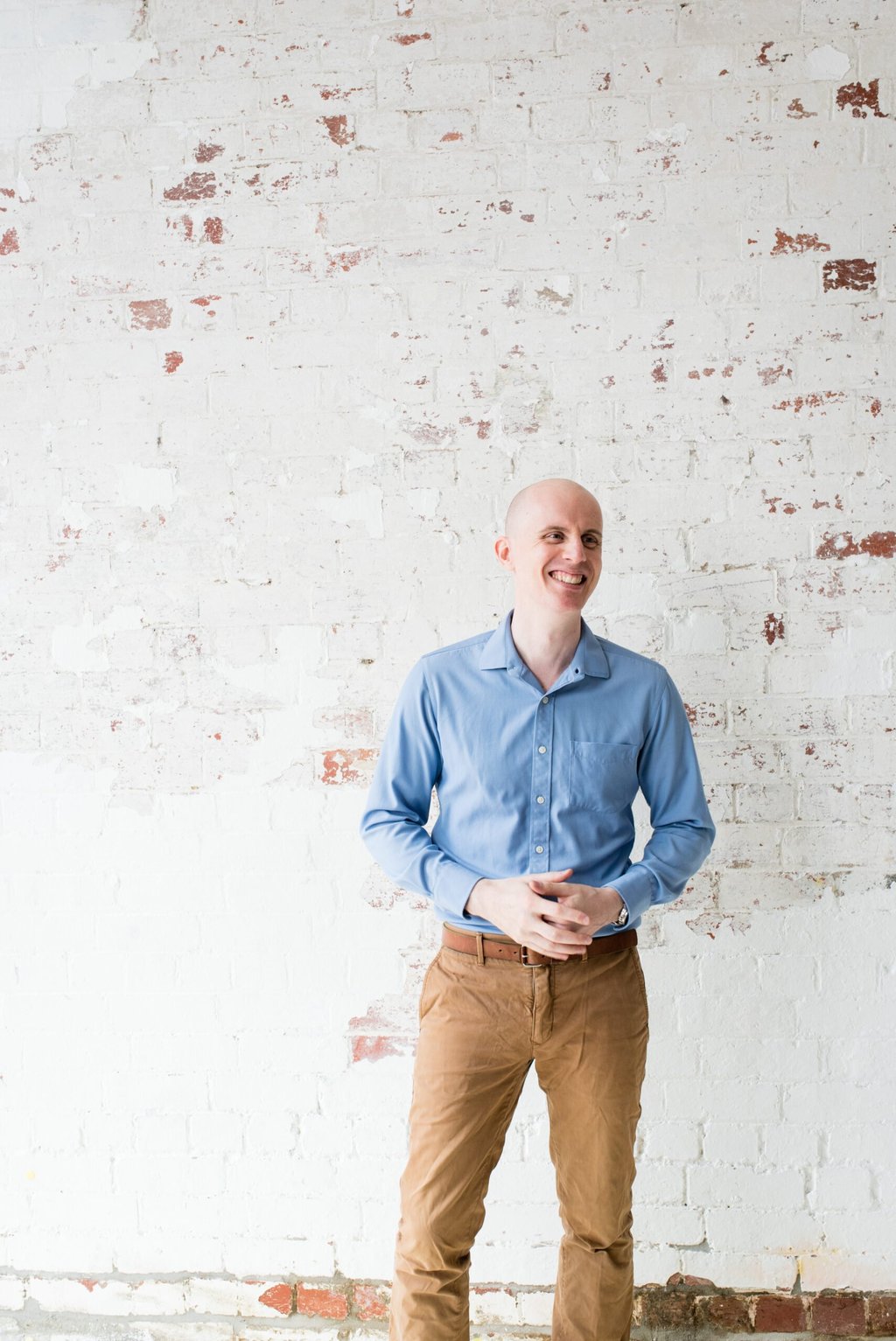 jabe-brown-press-standing-portrait male practitioner standing in front of brick wall painted white hands clasped in front