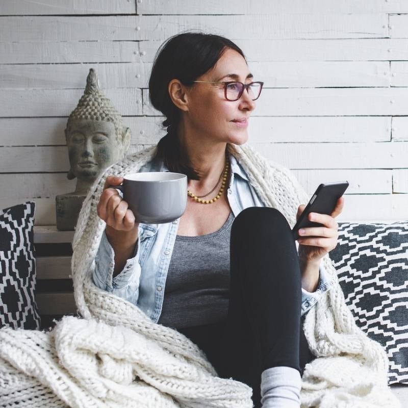 a woman sitting on a bench holding a coffee cup and a phone