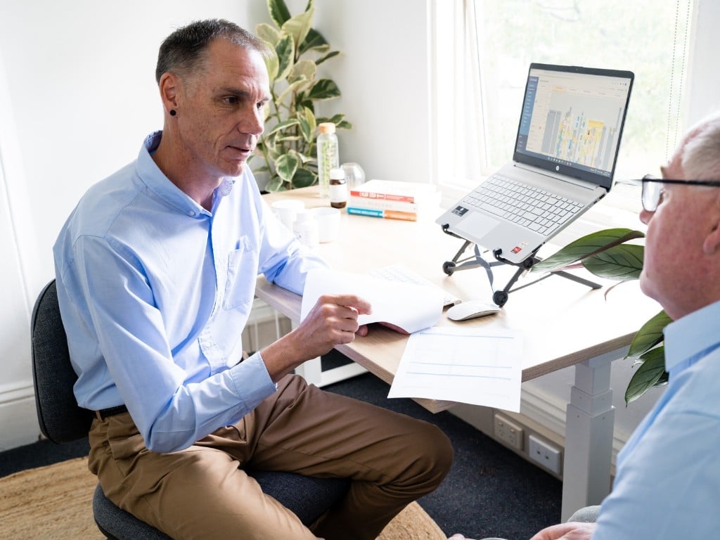 male functional medicine practitioner in clinic consulting with male patient laptop open