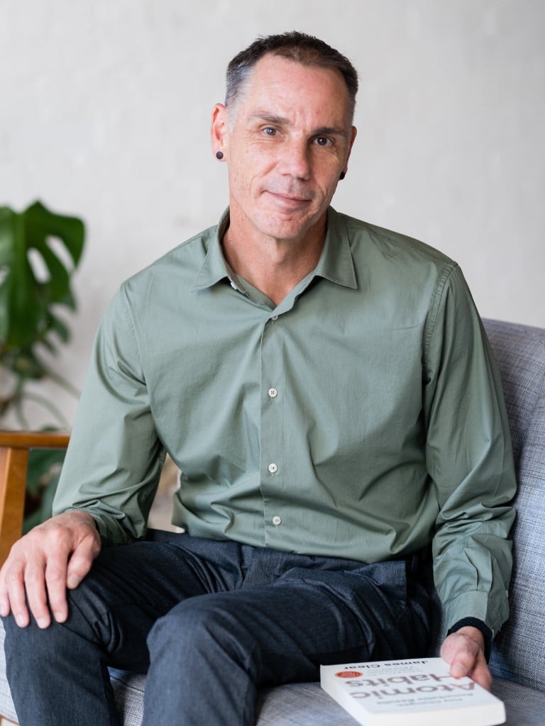 male functional medicine practitioner sitting on armchair with atomic habits book held in hand