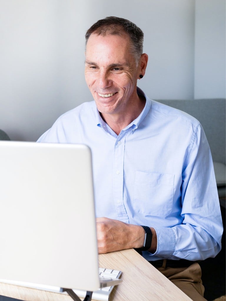 male functional medicine practitioner sitting at desk in front of lap top smiling