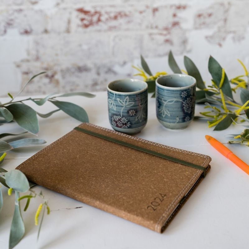 two ceramic tea cups leather bound journal surrounded by flowering wattle branches