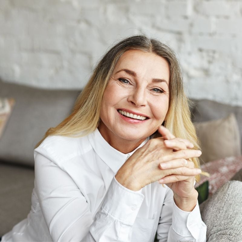 menopause-sweats-fatigue-weight-gain-case-study mature woman smiling sitting inside elbows on table hands clasped in front