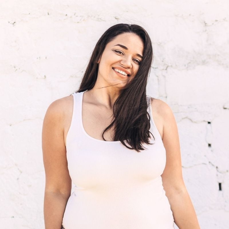 young woman standing against white brick wall in warm weather smiling