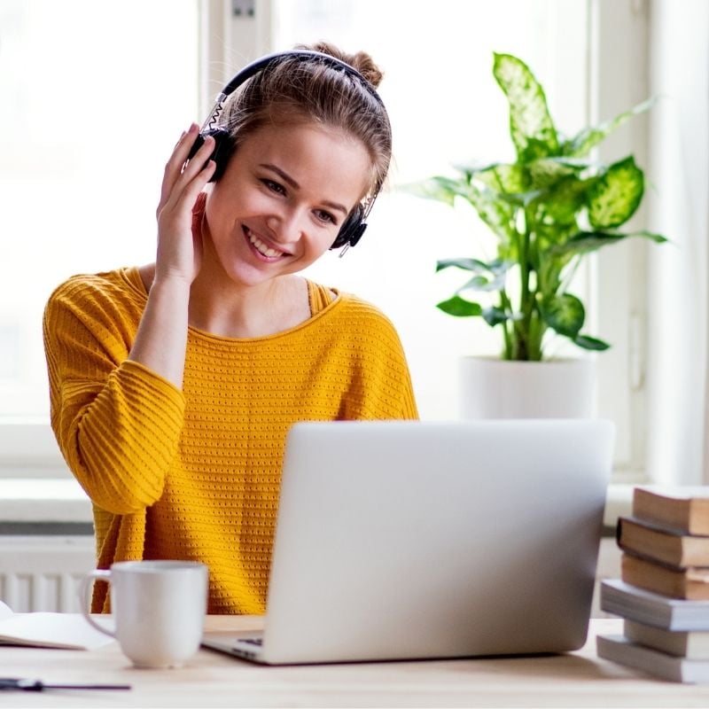 pms-functional-medicine-root-cause young woman sitting at table wearing headphones smiling looking at laptop