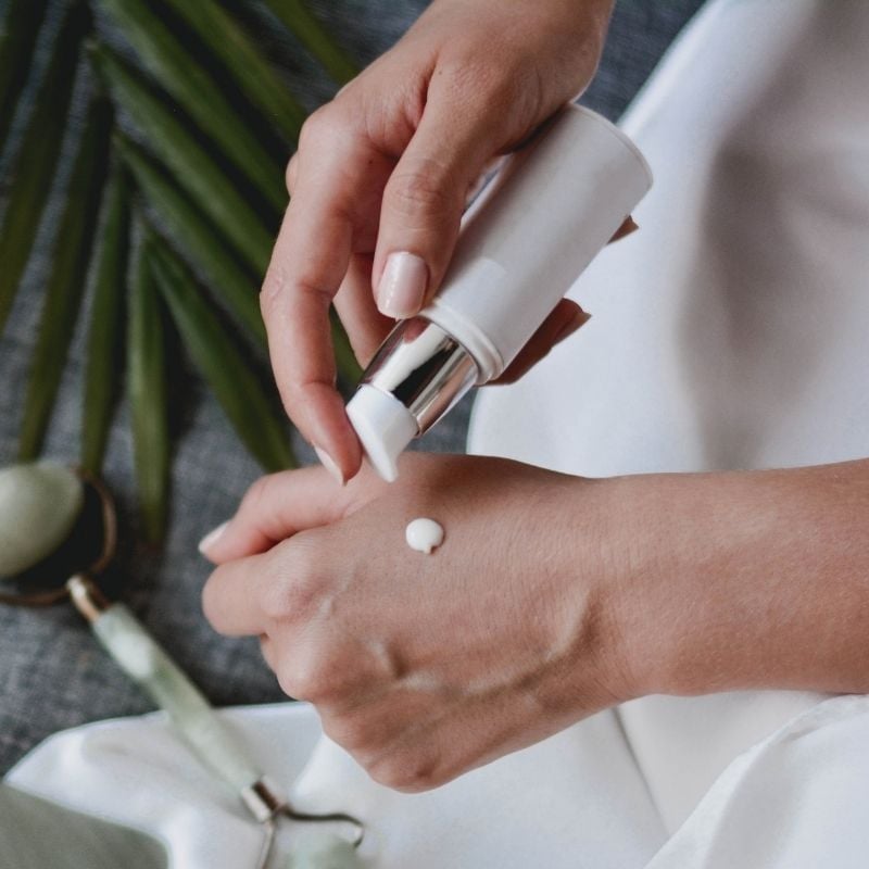 psoriasis-functional-medicine-hero woman dispensing drop moisturiser from pump bottle onto back of clear skin hands