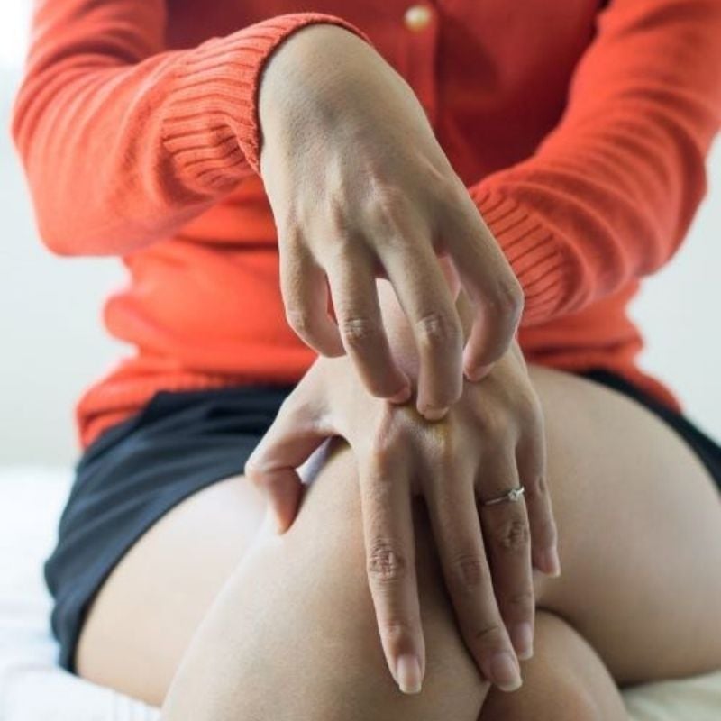 psoriasis-functional-medicine-root-cause woman sitting with legs crossed one hand scratching the back of the other