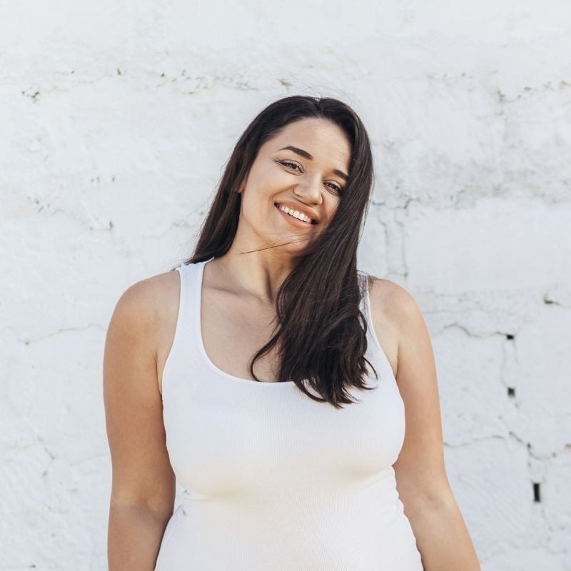 psoriatic-arthritis-functional-medicine-root-cause young woman standing outside with back to white brick wall smiling