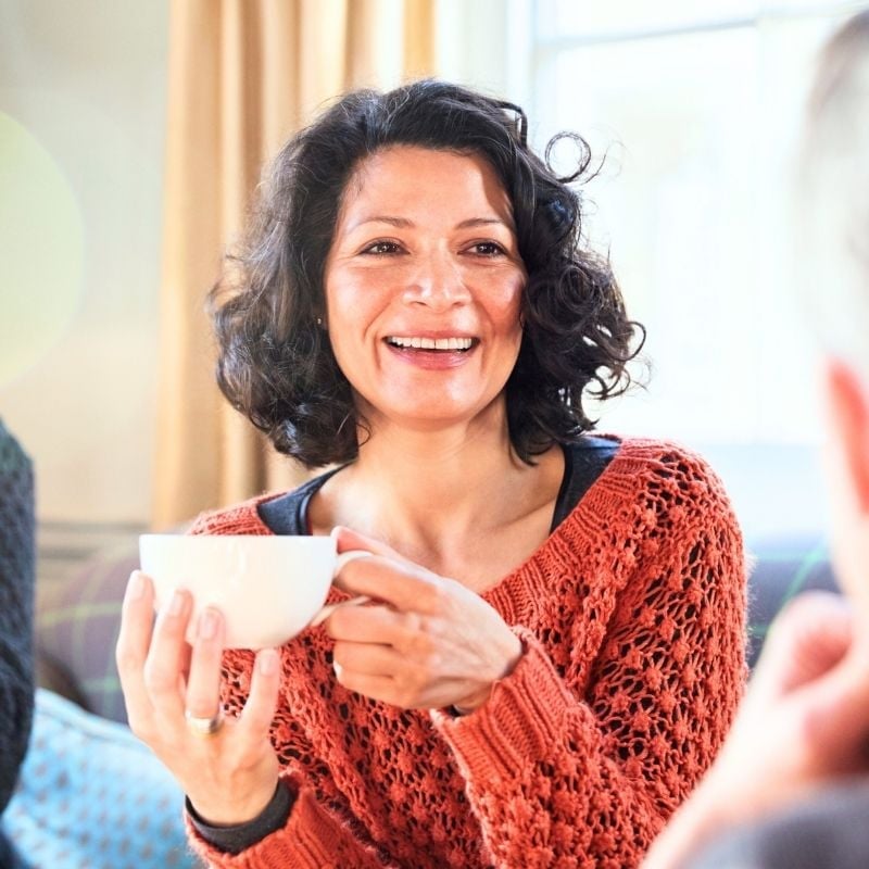 recurrent-uti-functional-medicine-root-cause middle aged woman sitting inside smiling holding cup of tea