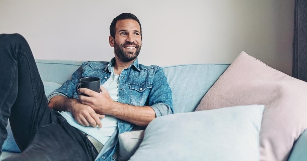 middle aged man relaxed on couch holding cup of tea smiling