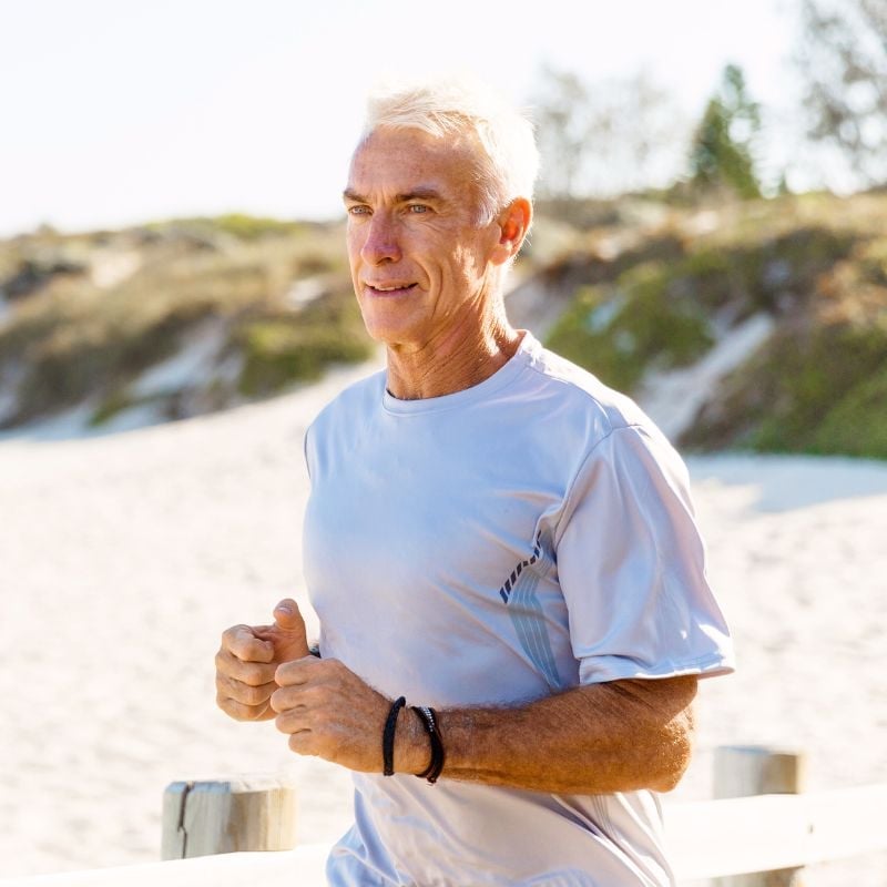 mature male running on beach with grass covered dunes in background