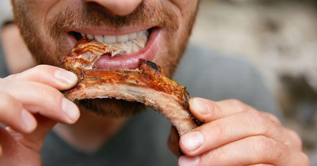 close up profile of man ripping meat of chop bone with his teeth