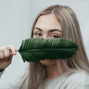 profile young woman holding dark green plant frond over nose mouth