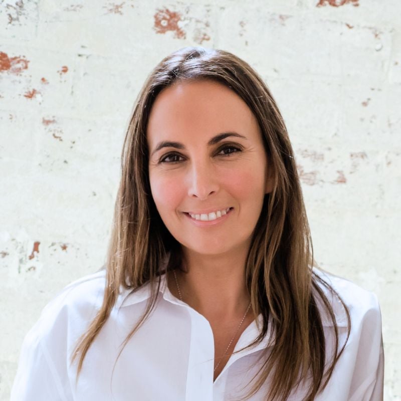 female health coach standing against white brick wall smiling
