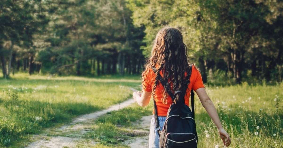 young woman in walking down dirt track lined with tall grass trees