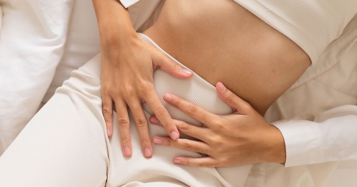 woman lying on back wearing pants crop top with hands resting across stomach