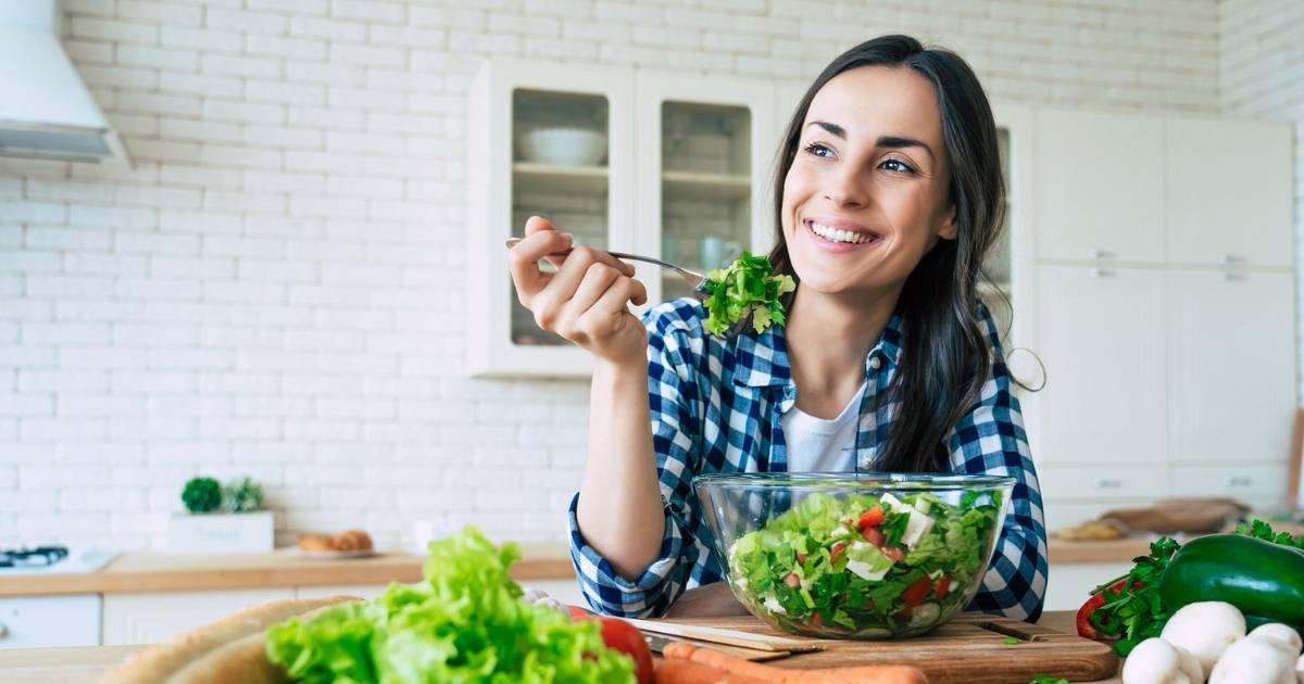 young woman sitting at table with large bowl salad for detoxification health