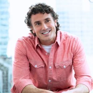 male sitting with arms resting on knees head tilted to the side smiling