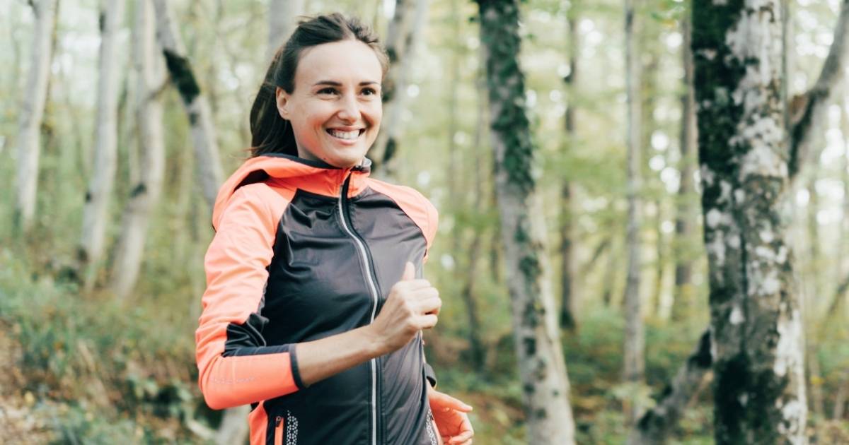 middle aged woman with energy smiling jogging in nature