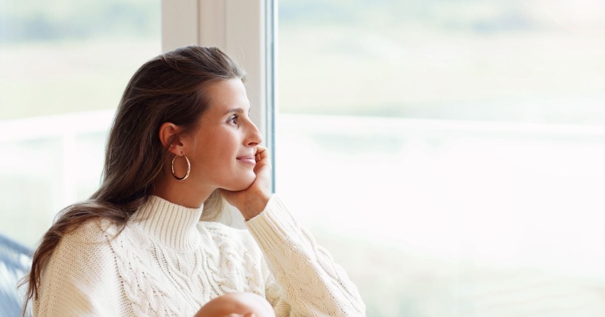 middle aged woman standing with sun on her face looking out to the ocean